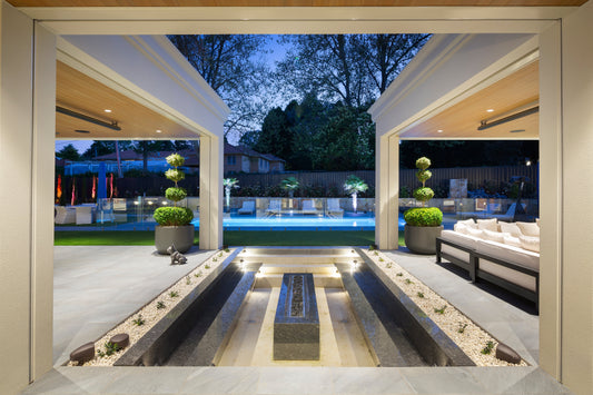 Covered outdoor entertaining area at dusk looking through to a lit pool, water feature and garden lighting